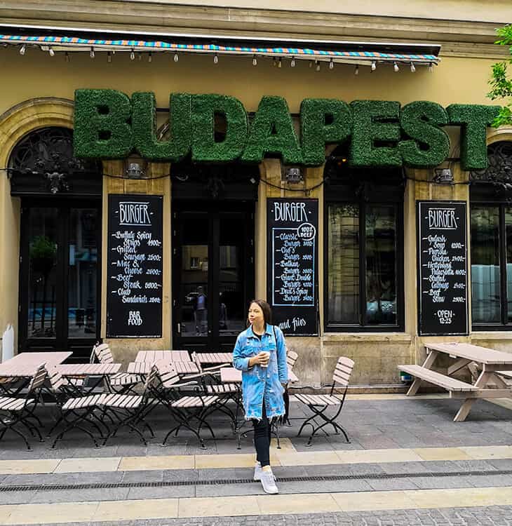 Girl walking in front of Budapest sing on a restaurant
