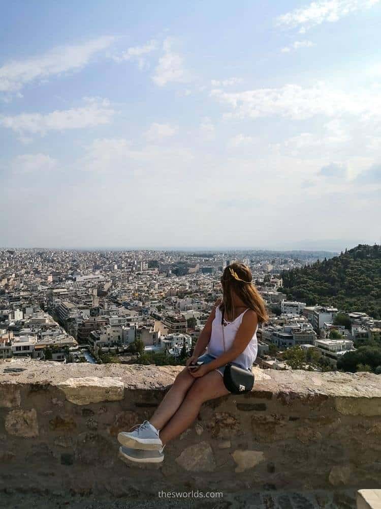 Girl looking at Athens city center while sitting on Acropolis walls
