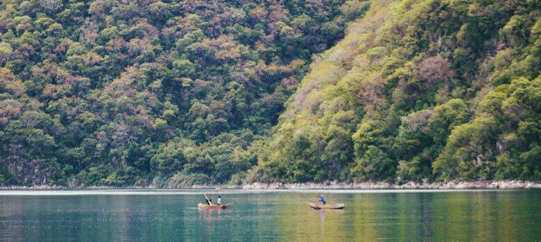 People in boats in lake next to tree mountain in Guatemala